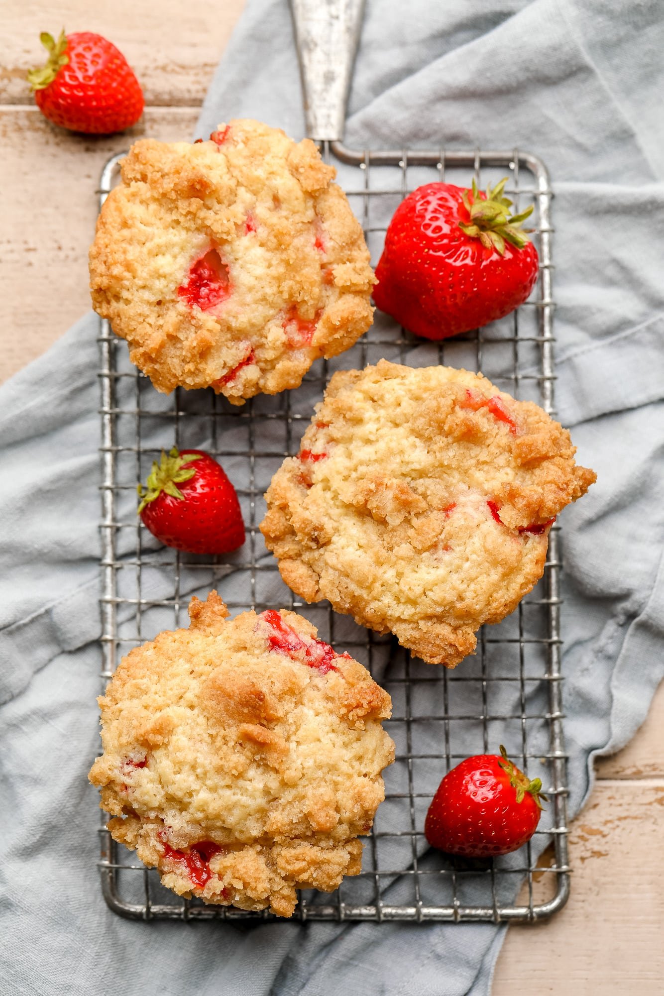 3 baked strawberry muffins on a small wire rack surrounded by strawberries.