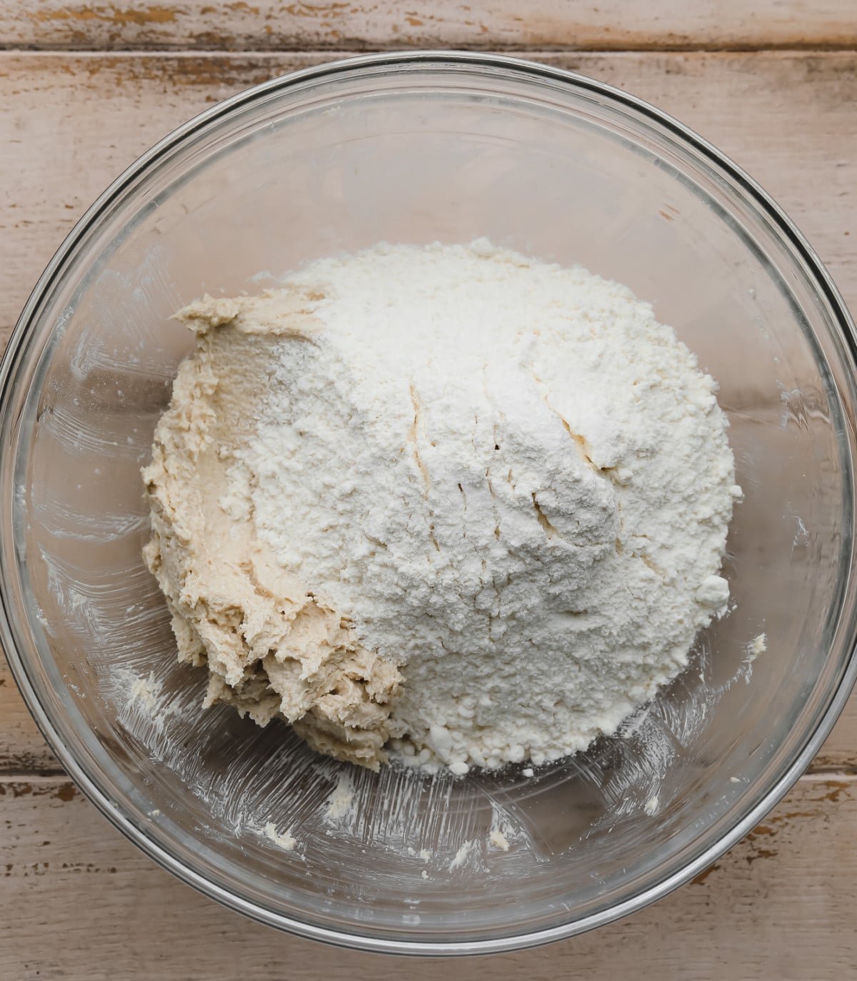 flour on top of butter sugar mixture in clear bowl