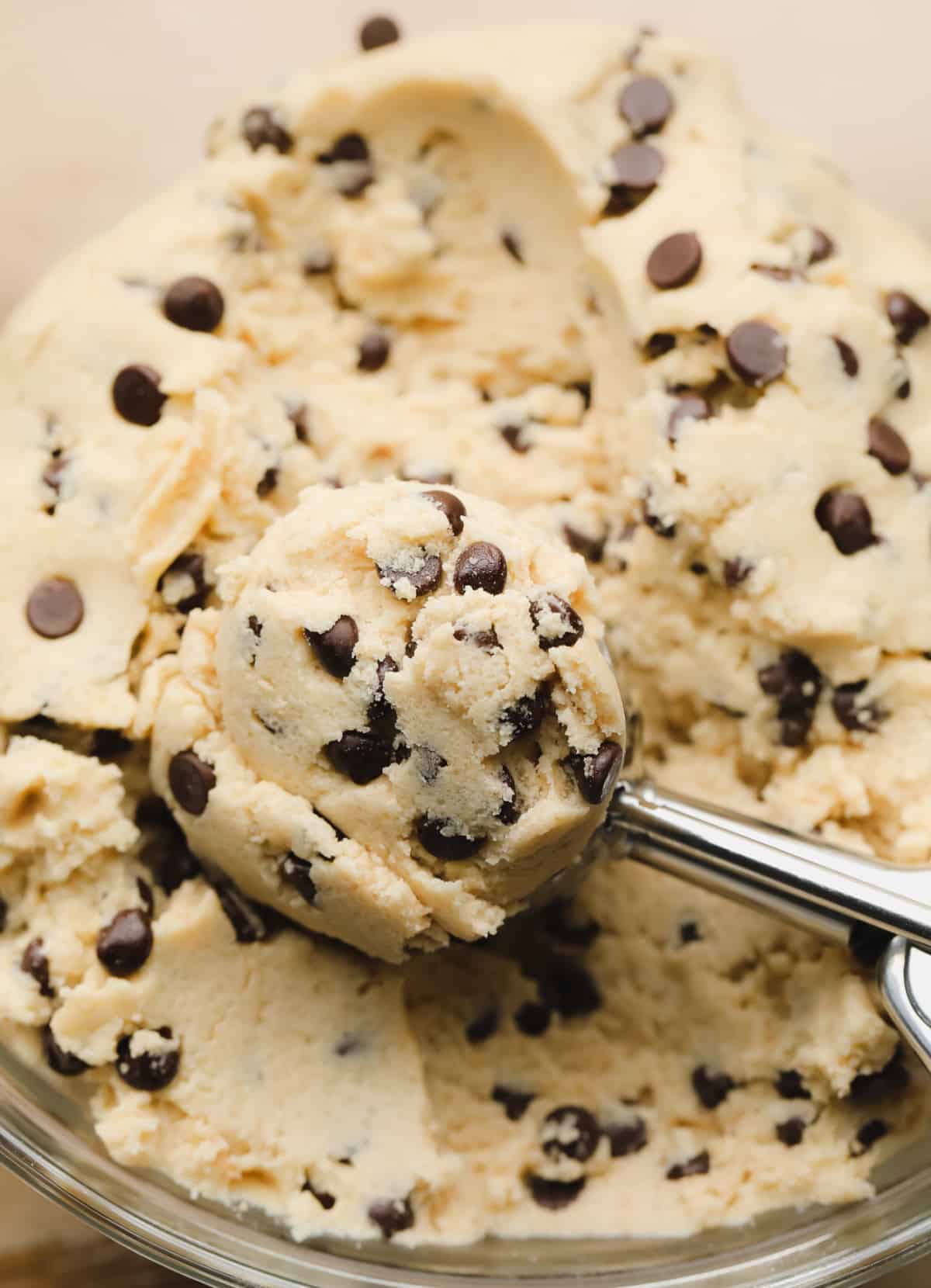 clear bowl of vegan cookie dough being scooped with a cookie scoop