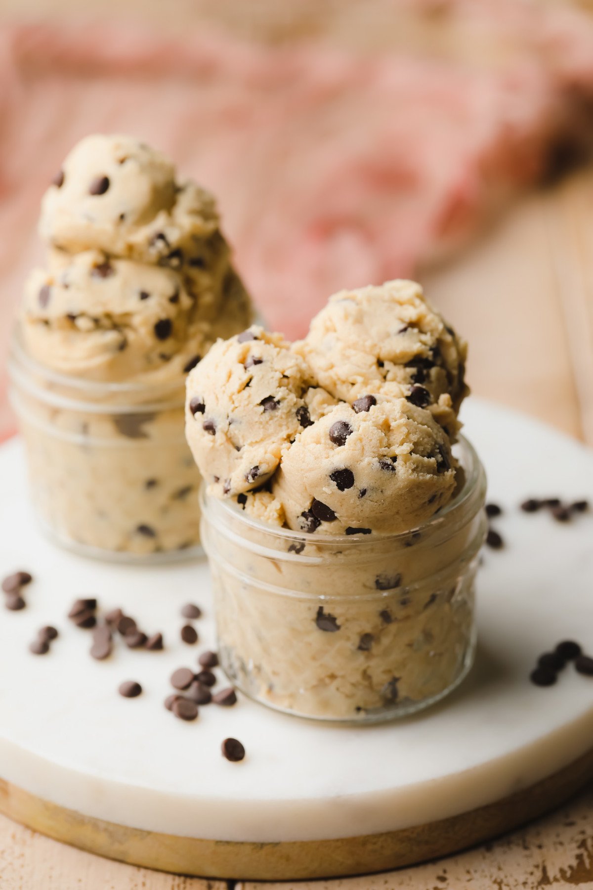 scoops of cookie dough in glass jars on round white marble board, pink towel in background