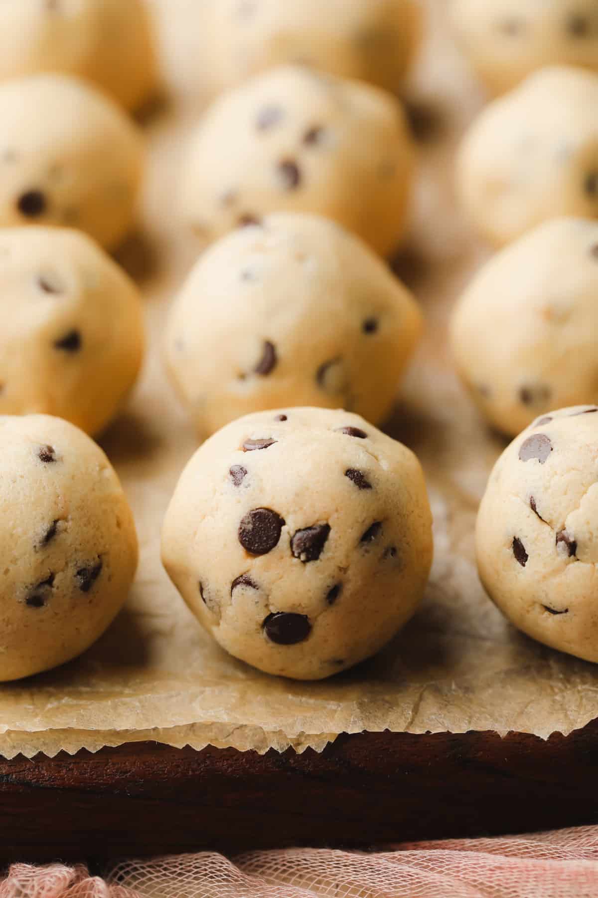 cookie dough balls in rows on a wood board with light brown paper underneath