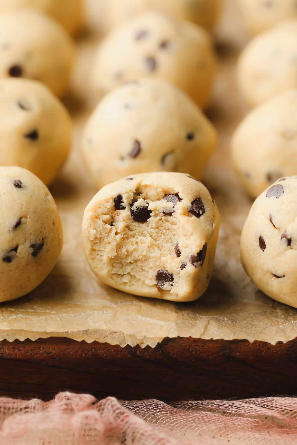 many balls of vegan cookie dough with one having had a bite taken out of it showing middle