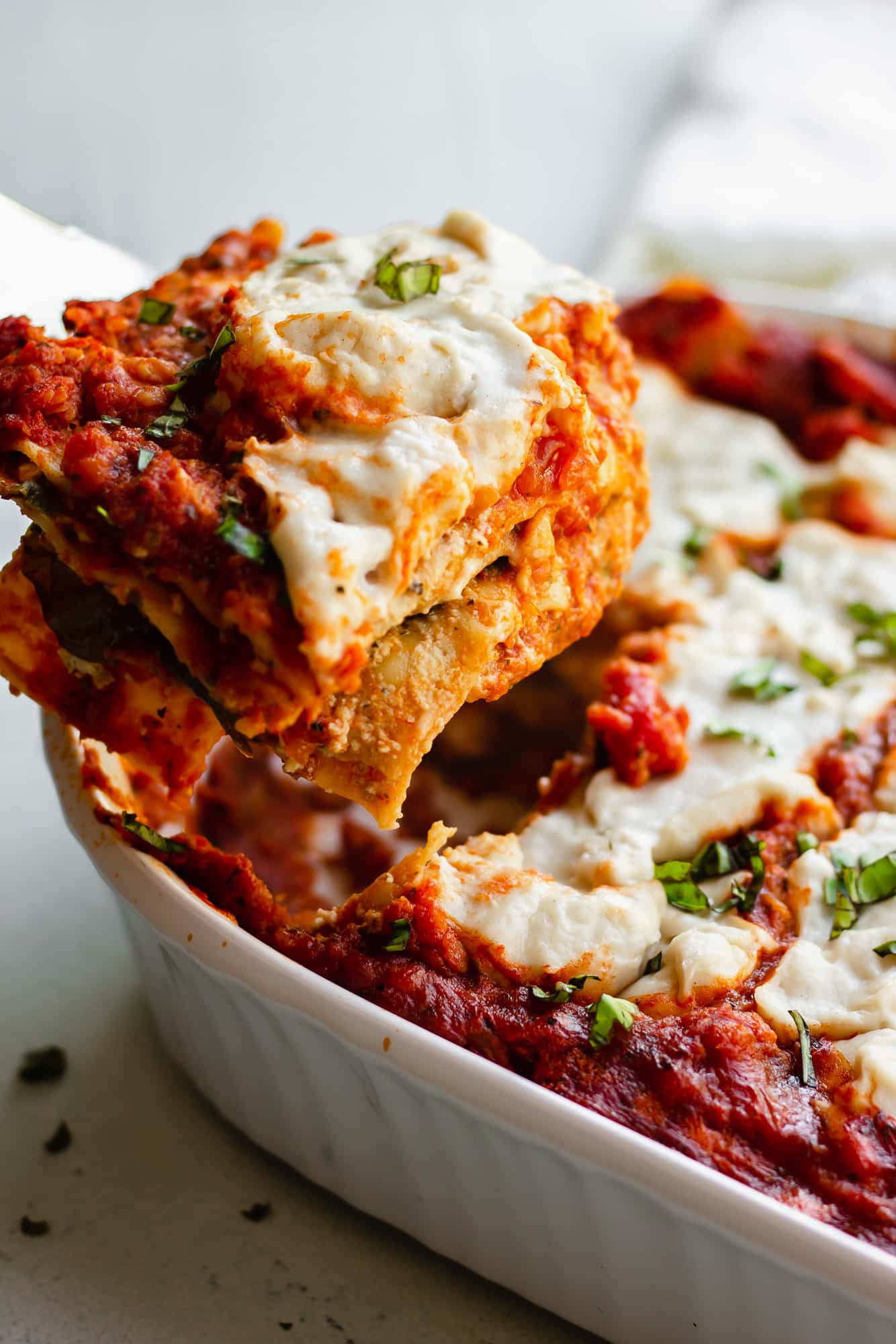 a slice of vegan lasagna being lifted from a white casserole dish.