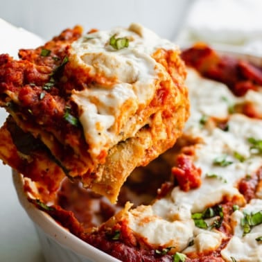 a slice of vegan lasagna being lifted from a white casserole dish.