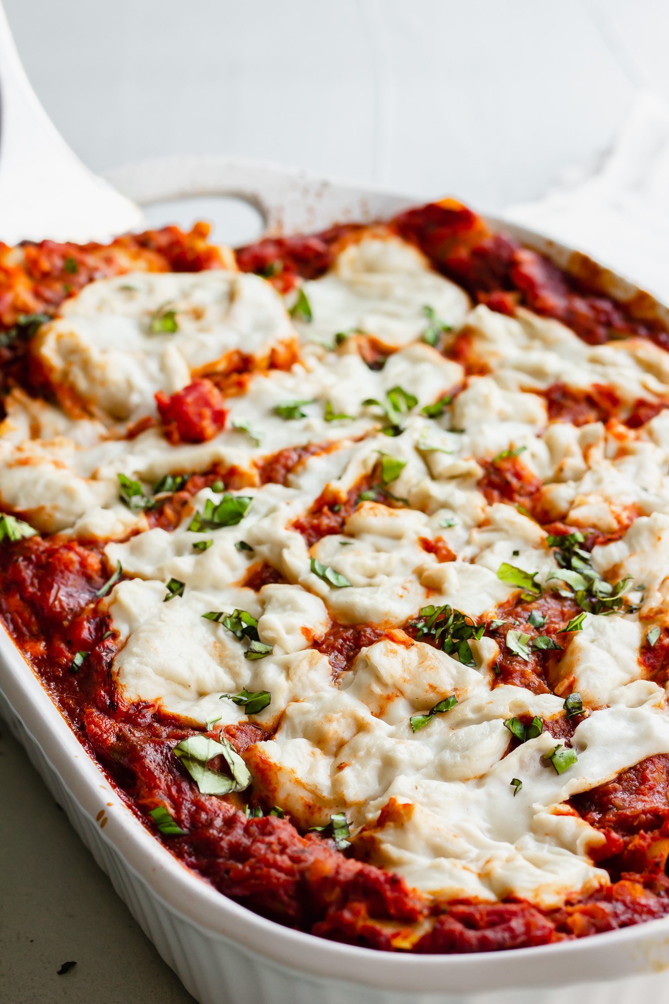 baked lasagna topped with vegan mozzarella cheese and red sauce in a white casserole dish.