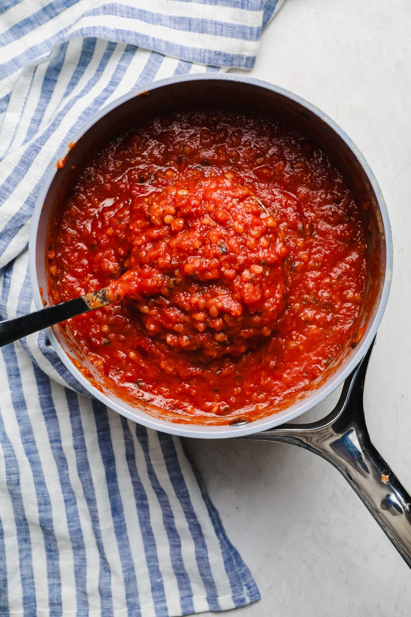 stirring cooked red lentils and marinara sauce in a white saucepan.