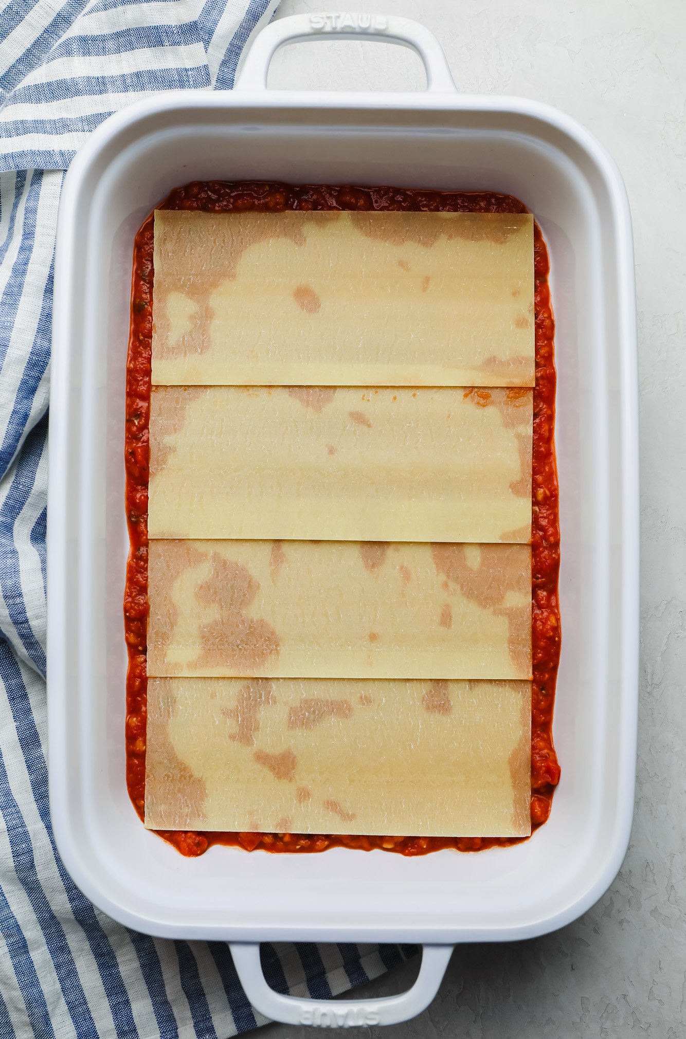 layering lasagna noodles on top of red sauce in a white casserole dish.
