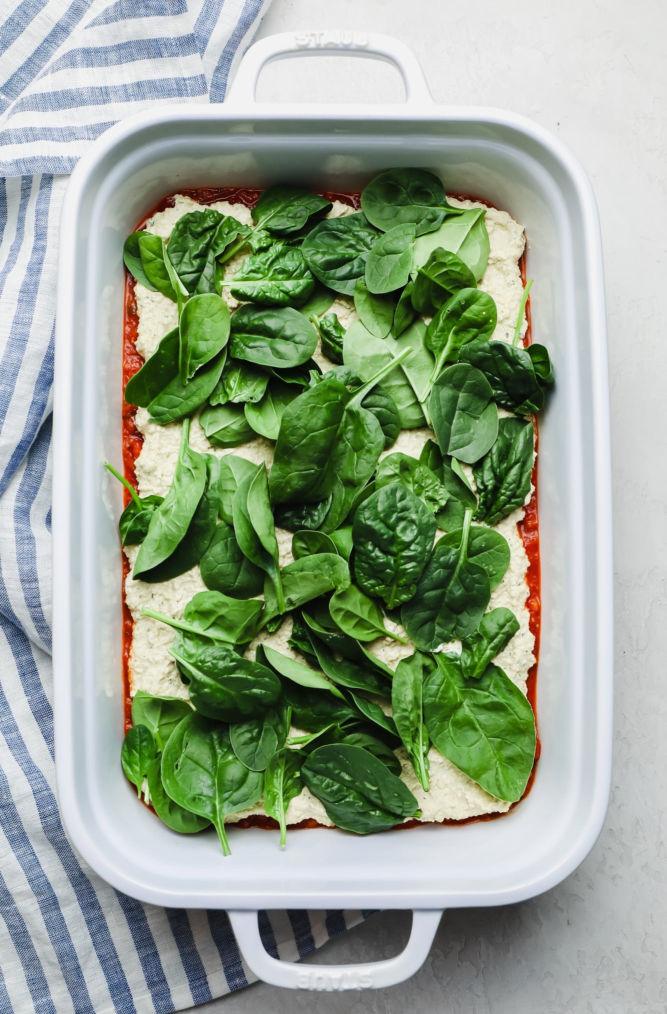 layering spinach into a vegan lasagna.