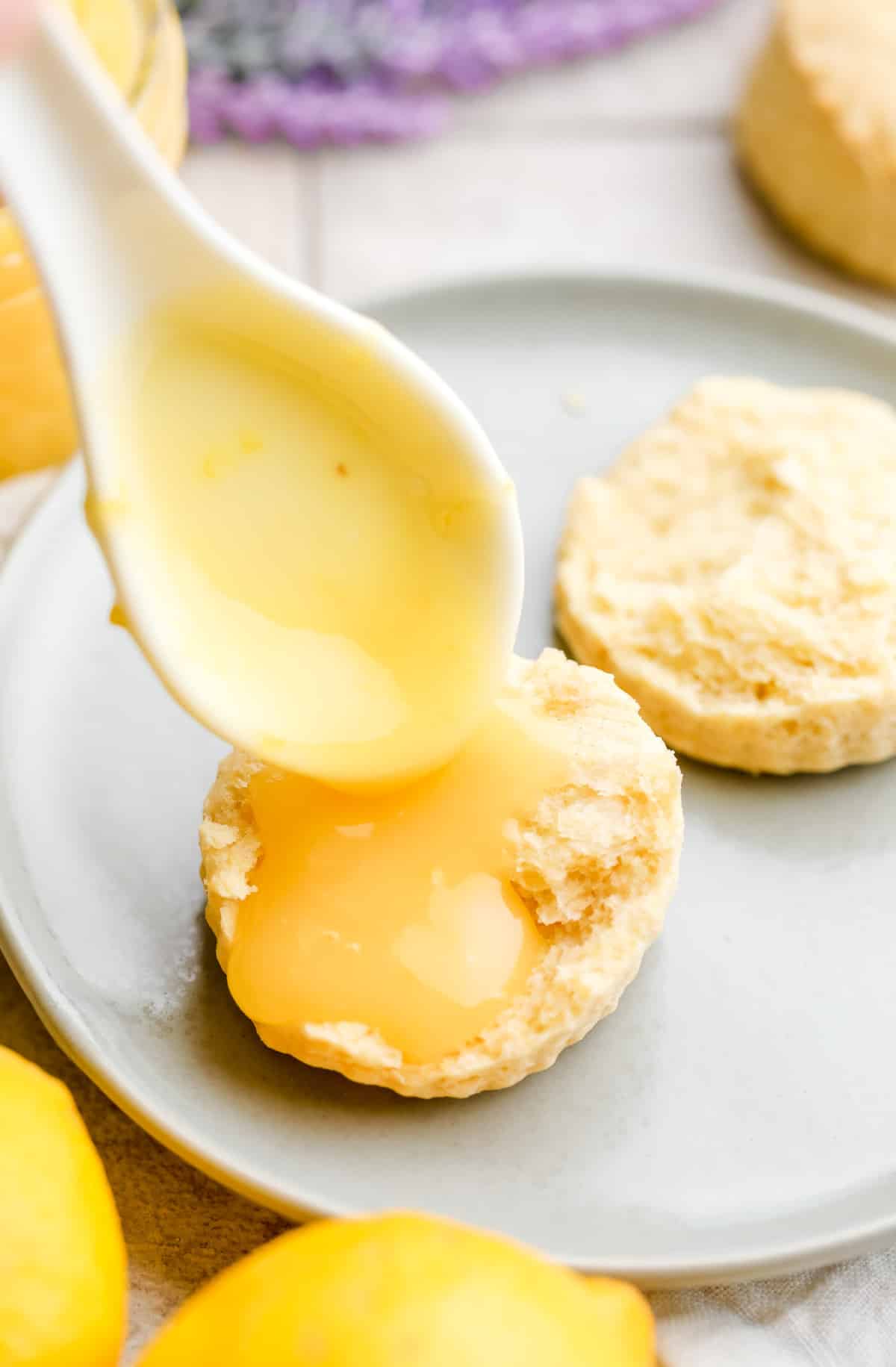 vegan lemon curd being spooned onto a plain round scone, lavender in background