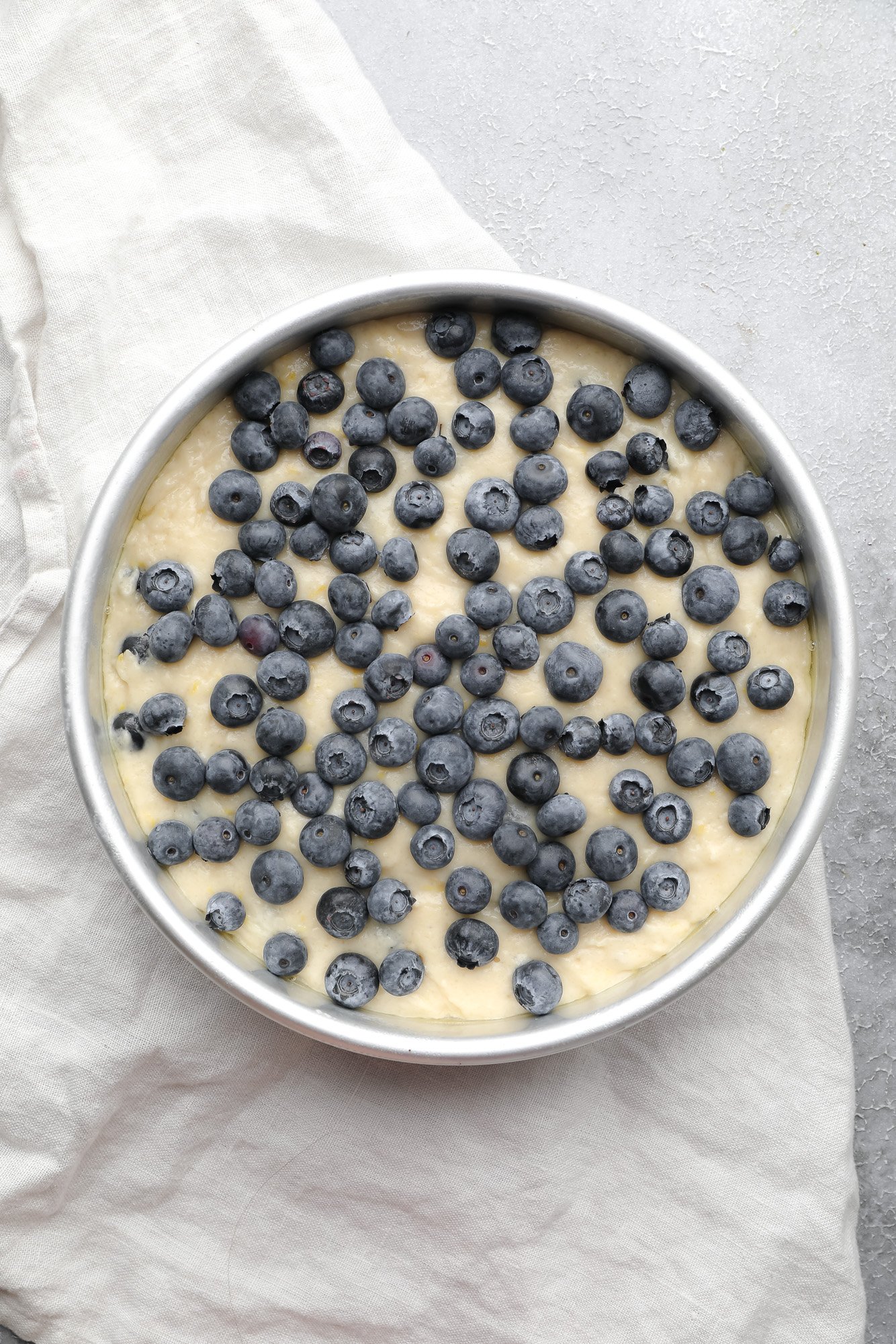 blueberry cake batter with fresh blueberries on top in a round metal cake pan.
