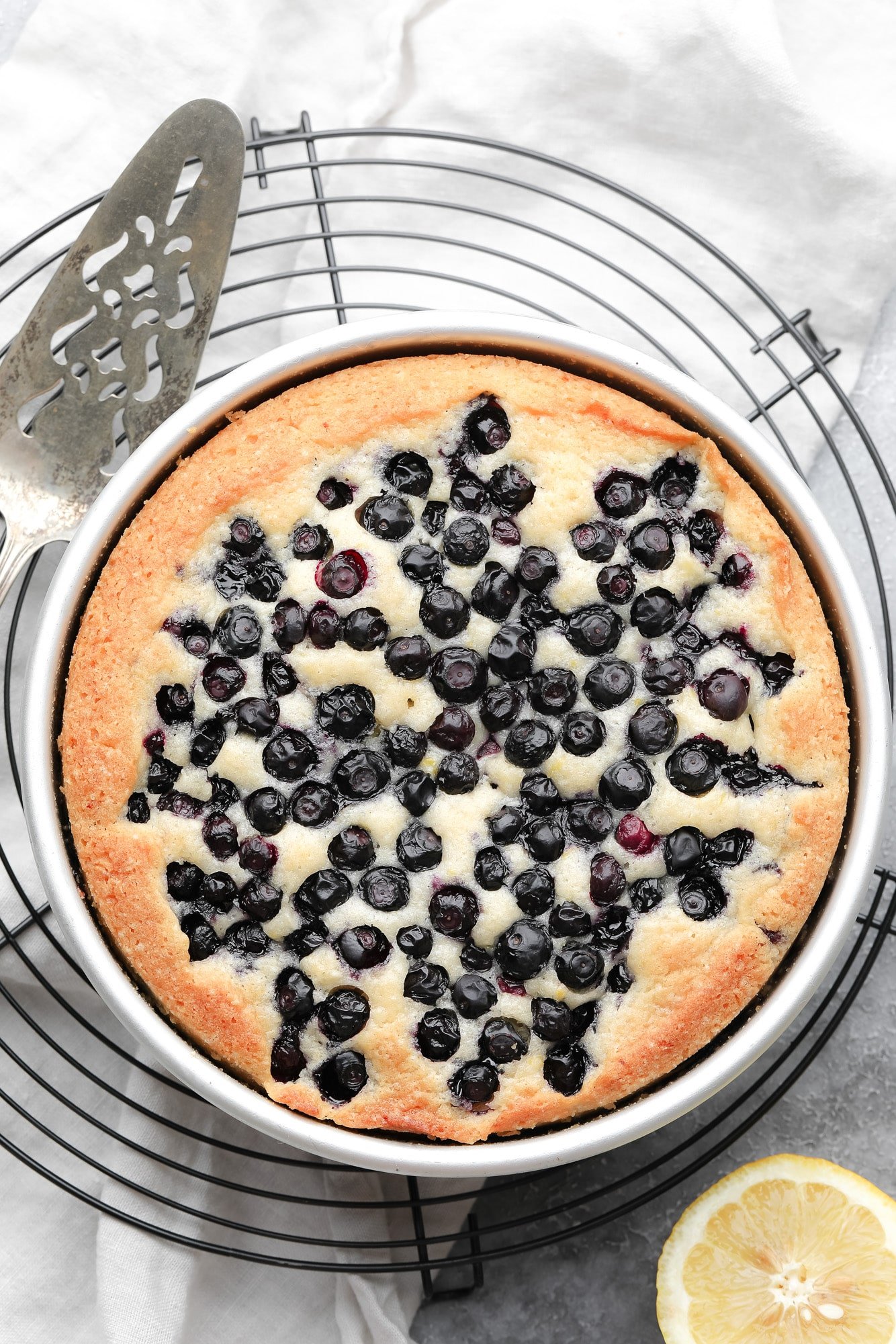 a baked vegan blueberry cake in a round metal pan.