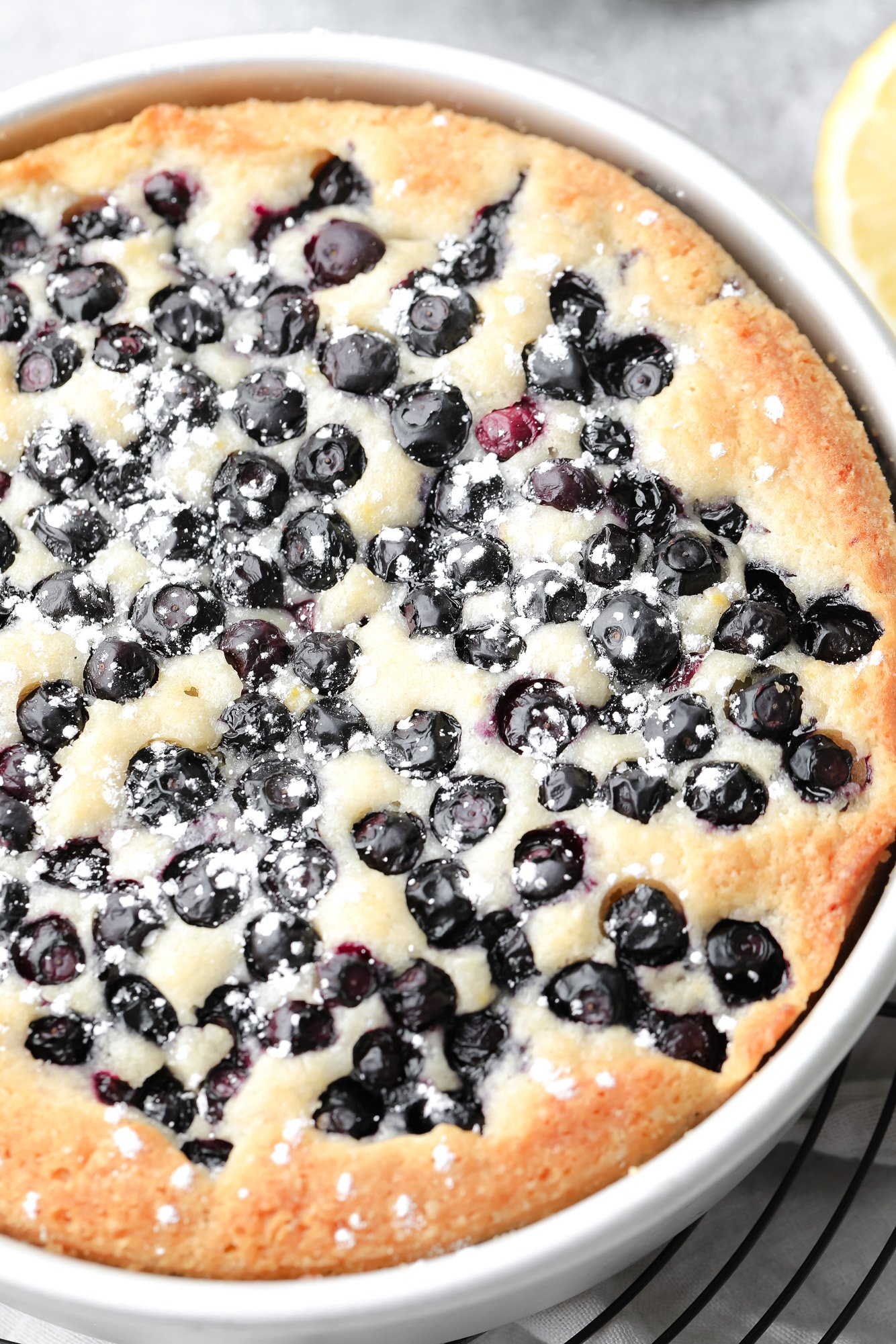 close up on a baked vegan blueberry cake dusted with powdered sugar.