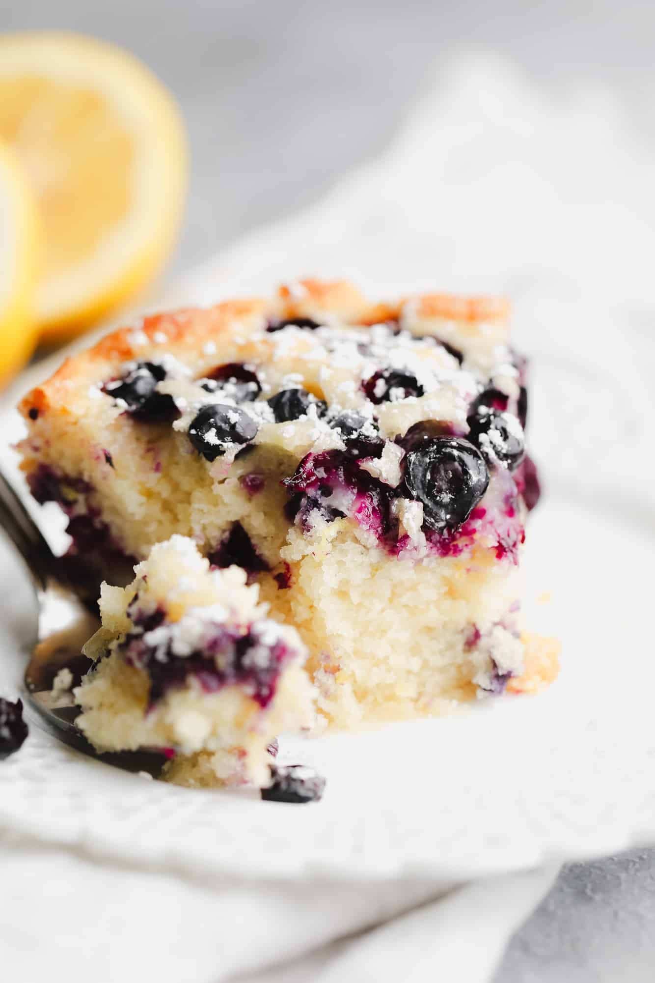 close up on a slice of vegan blueberry cake with a bite missing on a white plate.