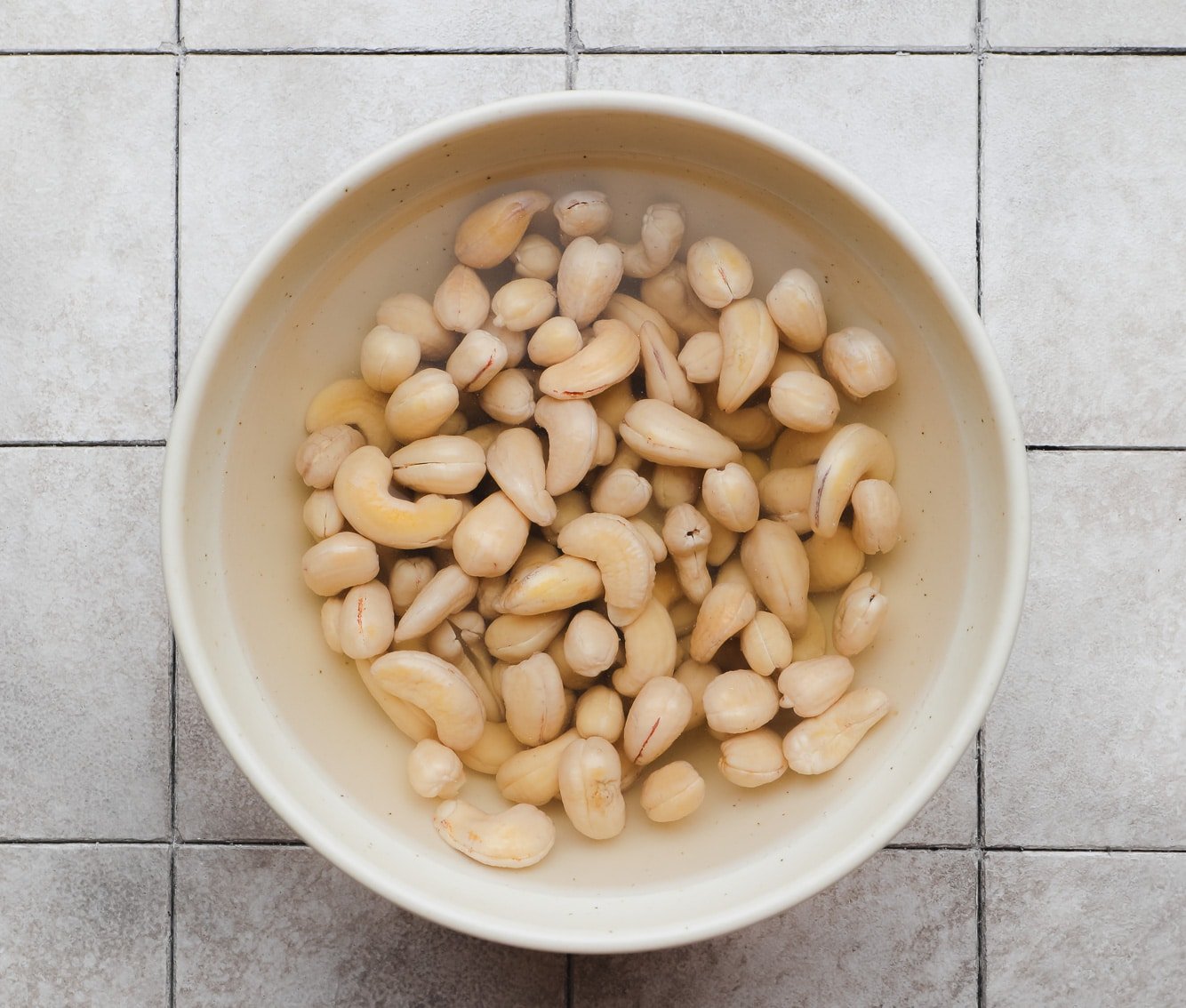 soaking cashews in water in a beige bowl.