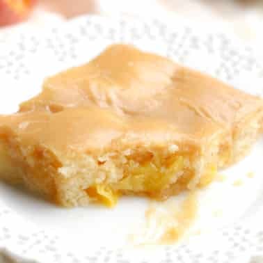 square image of a piece of peach cake with brown sugar icing on top on a white plate