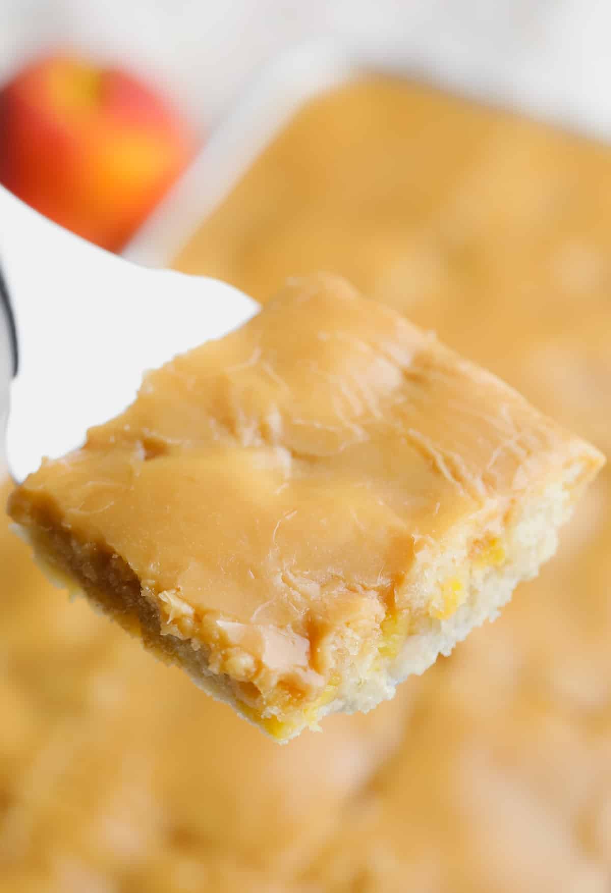 spatula holding a piece of sheet cake with peaches over a whole cake