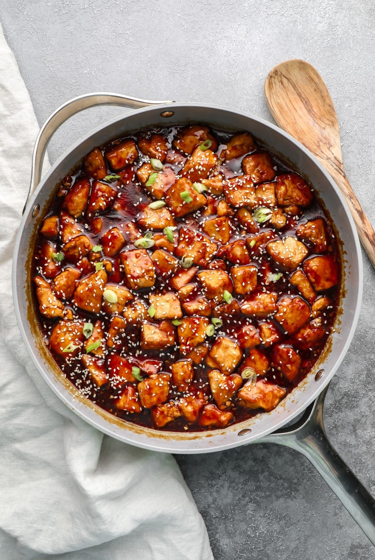 large grey pan with teriyaki tofu in it, chunked with sesame seeds and green onions