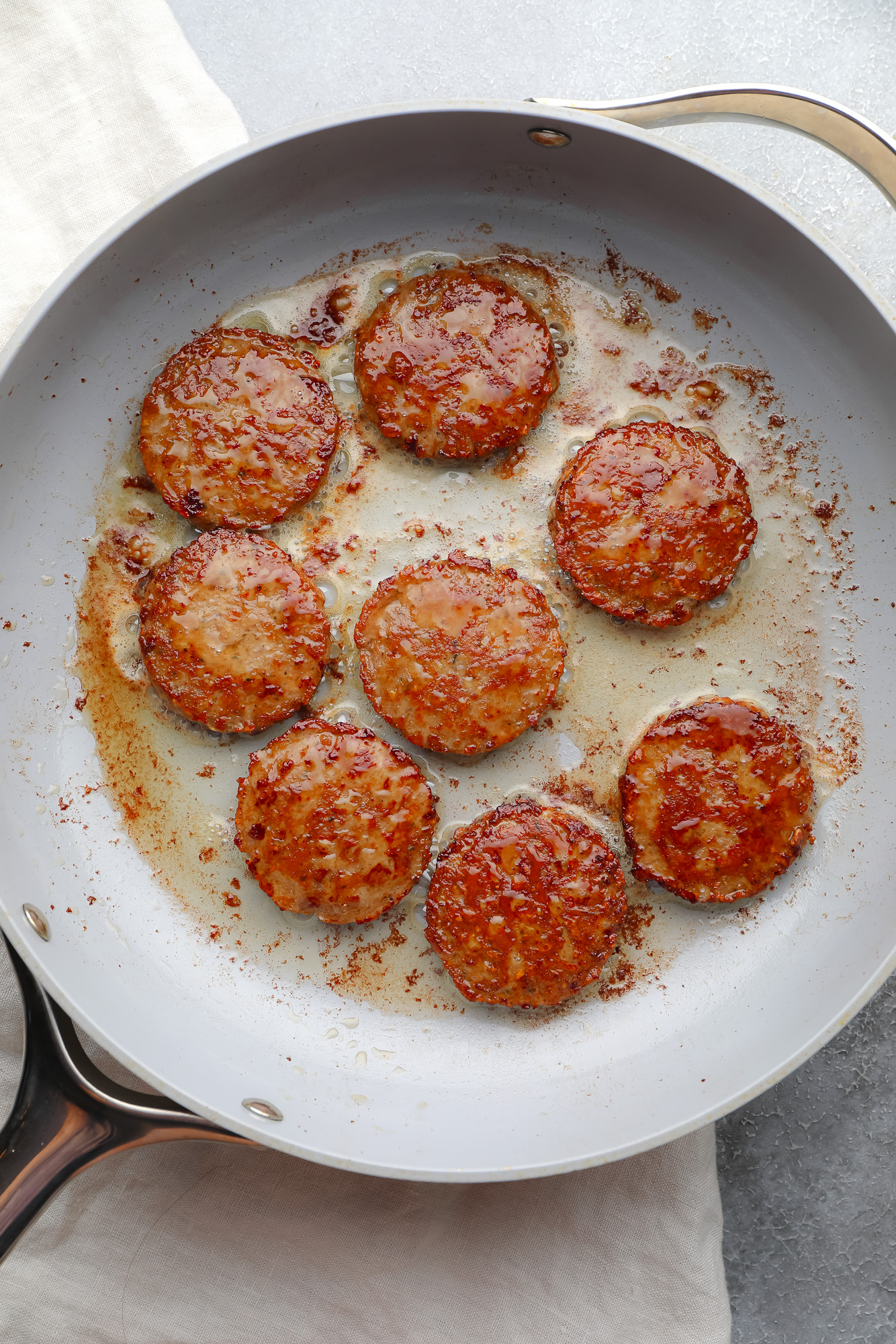 vegan breakfast sausage rounds cooking in a large grey skillet.