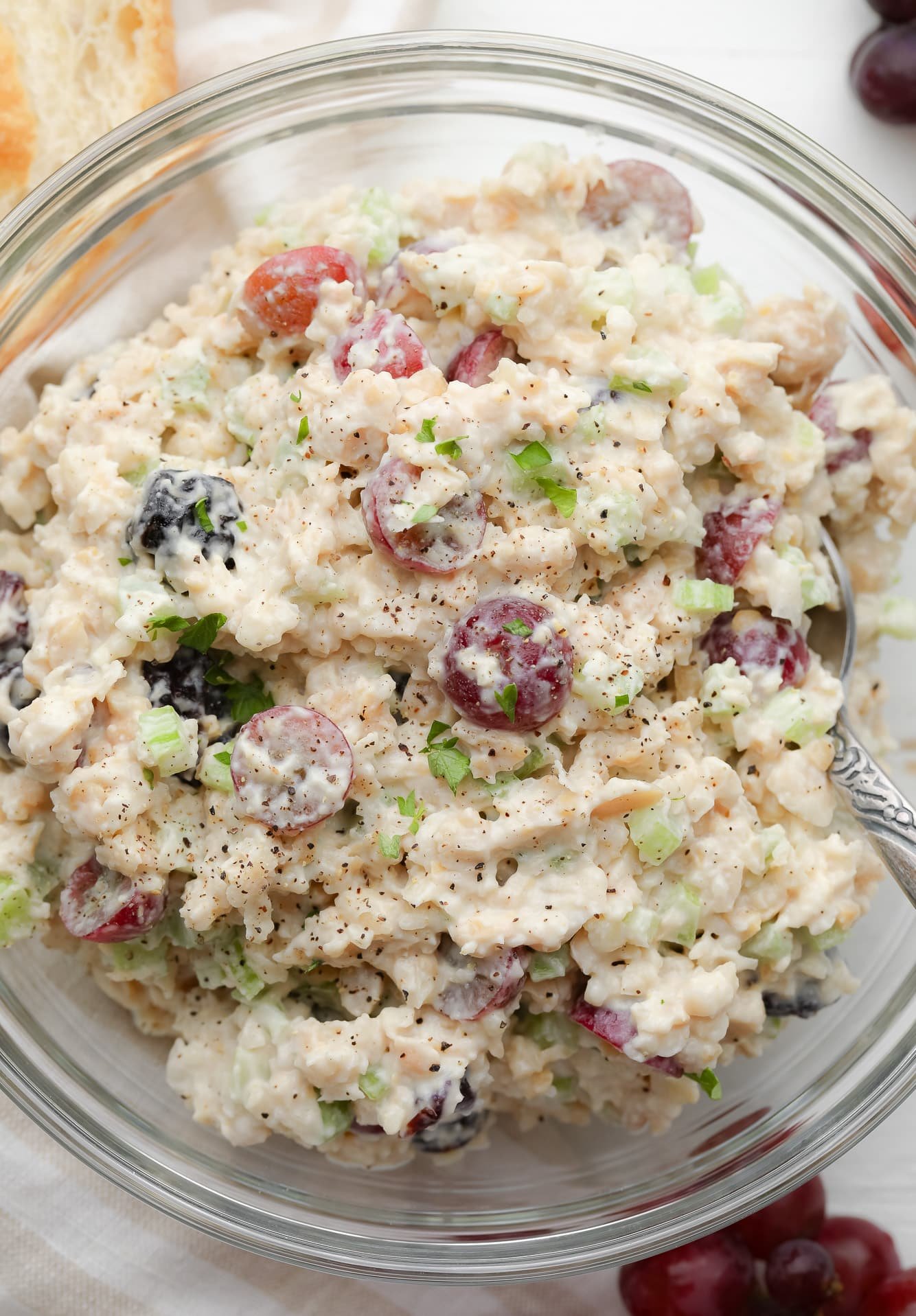 using a metal spoon to stir the ingredients for vegan chicken salad together in a large glass bowl.