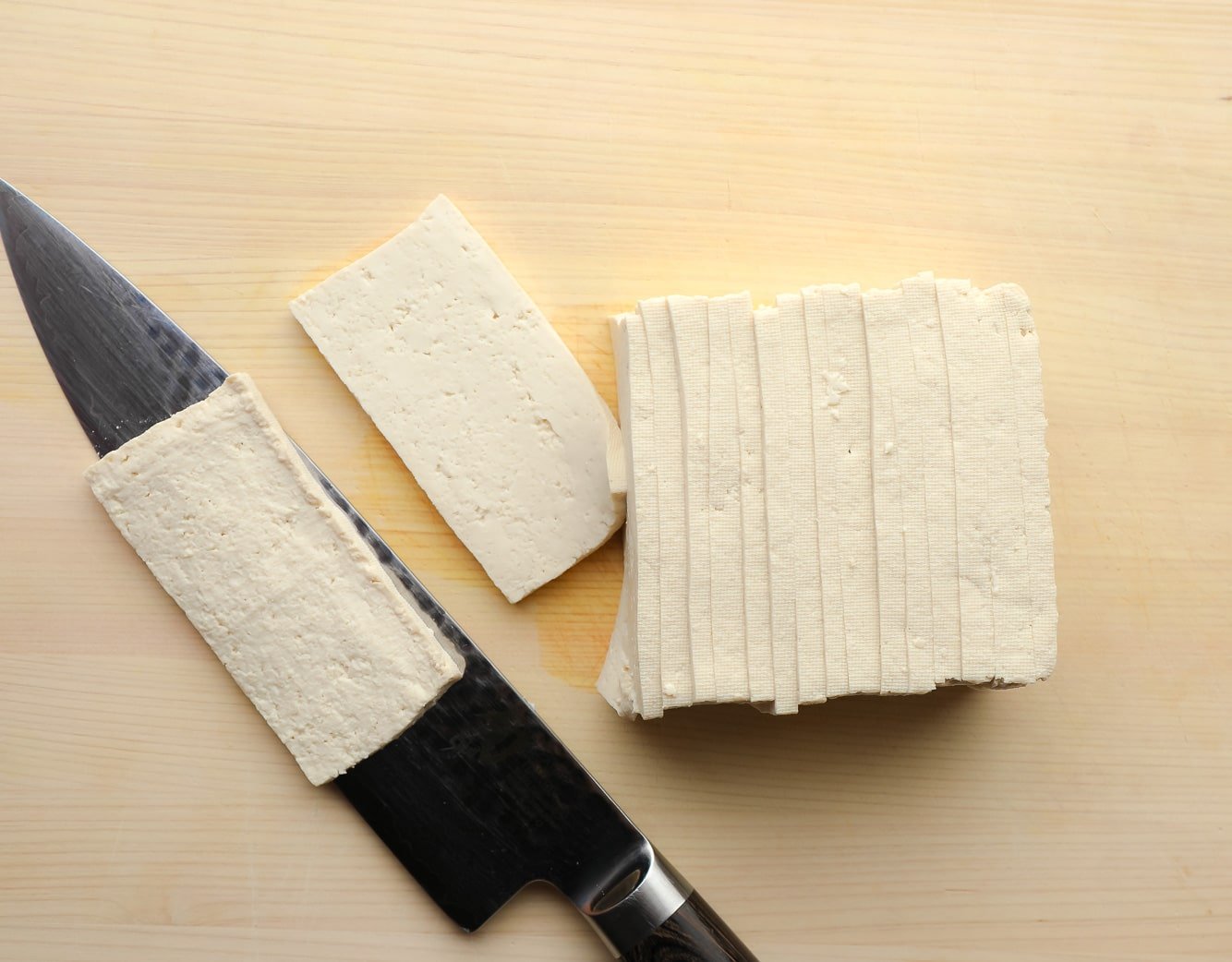 using a chef's knife to slice a brick of tofu into thin, rectangular strips.