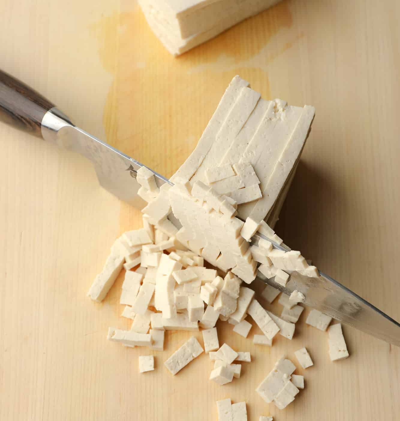 using a chef's knife to chop sliced tofu into very small squares.
