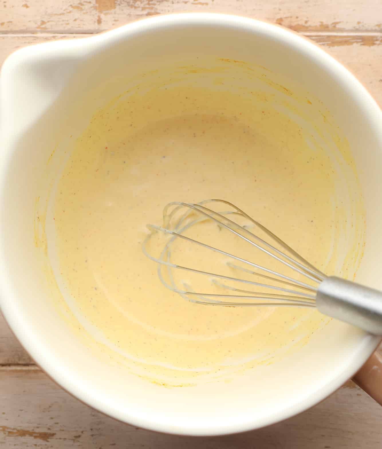 using a whisk to make a creamy yellow dressing in a white bowl for vegan egg salad.
