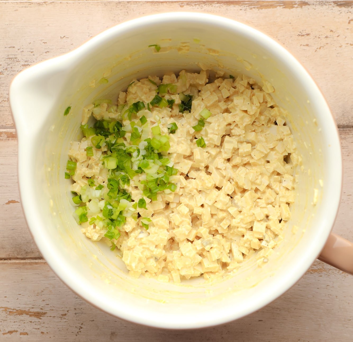 vegan egg salad topped with scallions in a large white bowl.