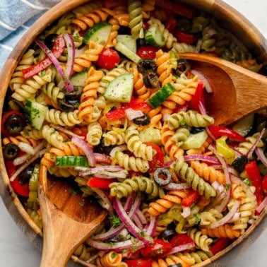square image of pasta salad in wood bowl with spoons in it