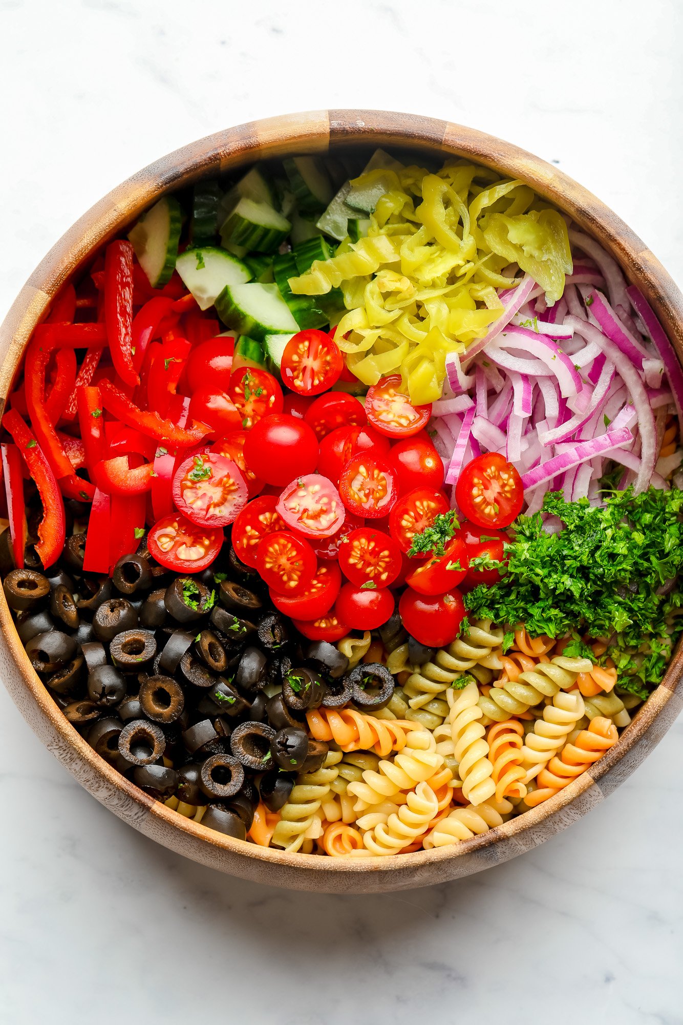 wood bowl on white background with pasta and vegetables not yet mixed for vegan pasta salad