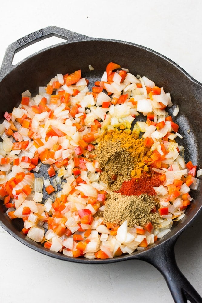 spices being added to a pan with peppers and onions