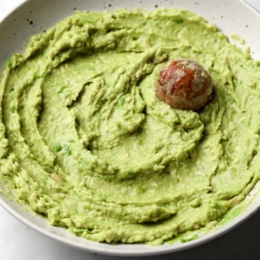 smooth and green avocado spread with the avocado seed on top in a beige bowl.