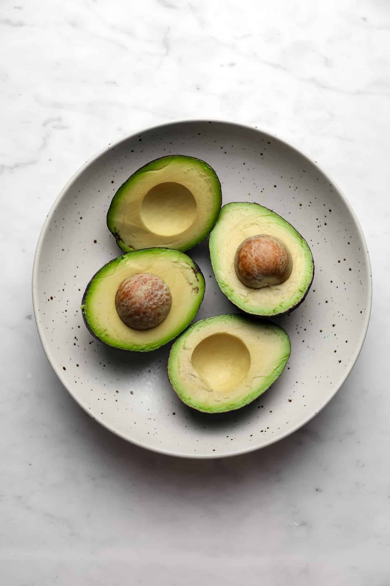 4 avocado halfs in a beige bowl.