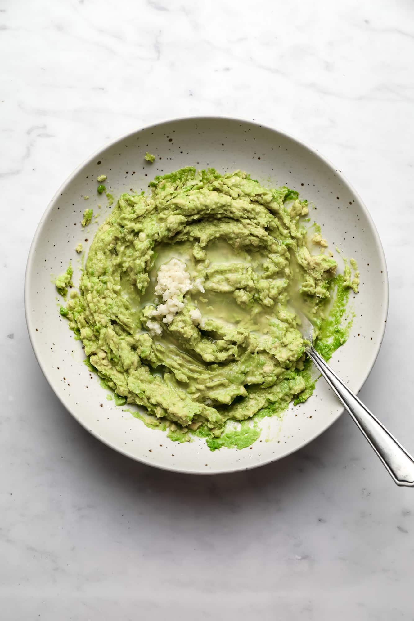using a spoon to stir minced garlic and lime juice into a bowl of mashed avocado.
