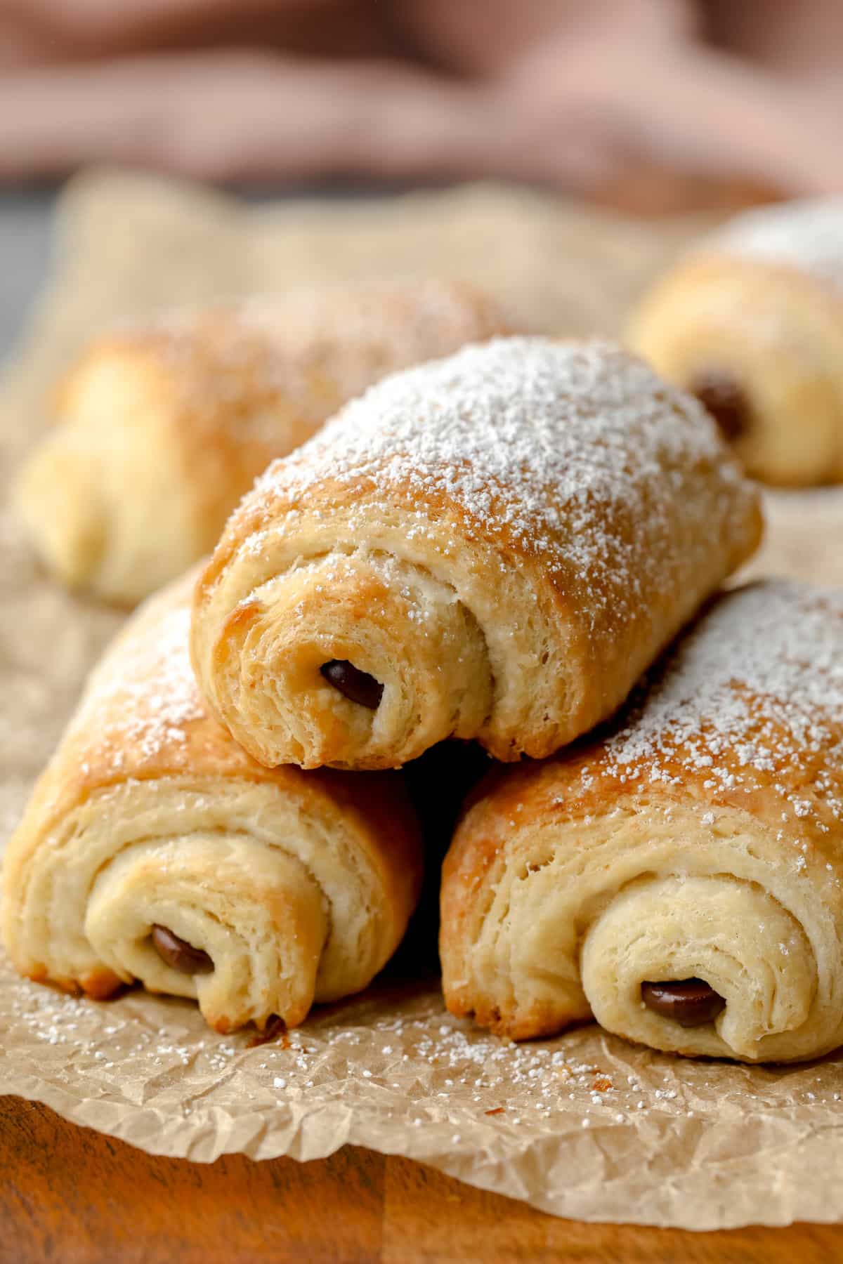 3 vegan pain au chocolat stacked on crinkly parchment paper with pink towel in background