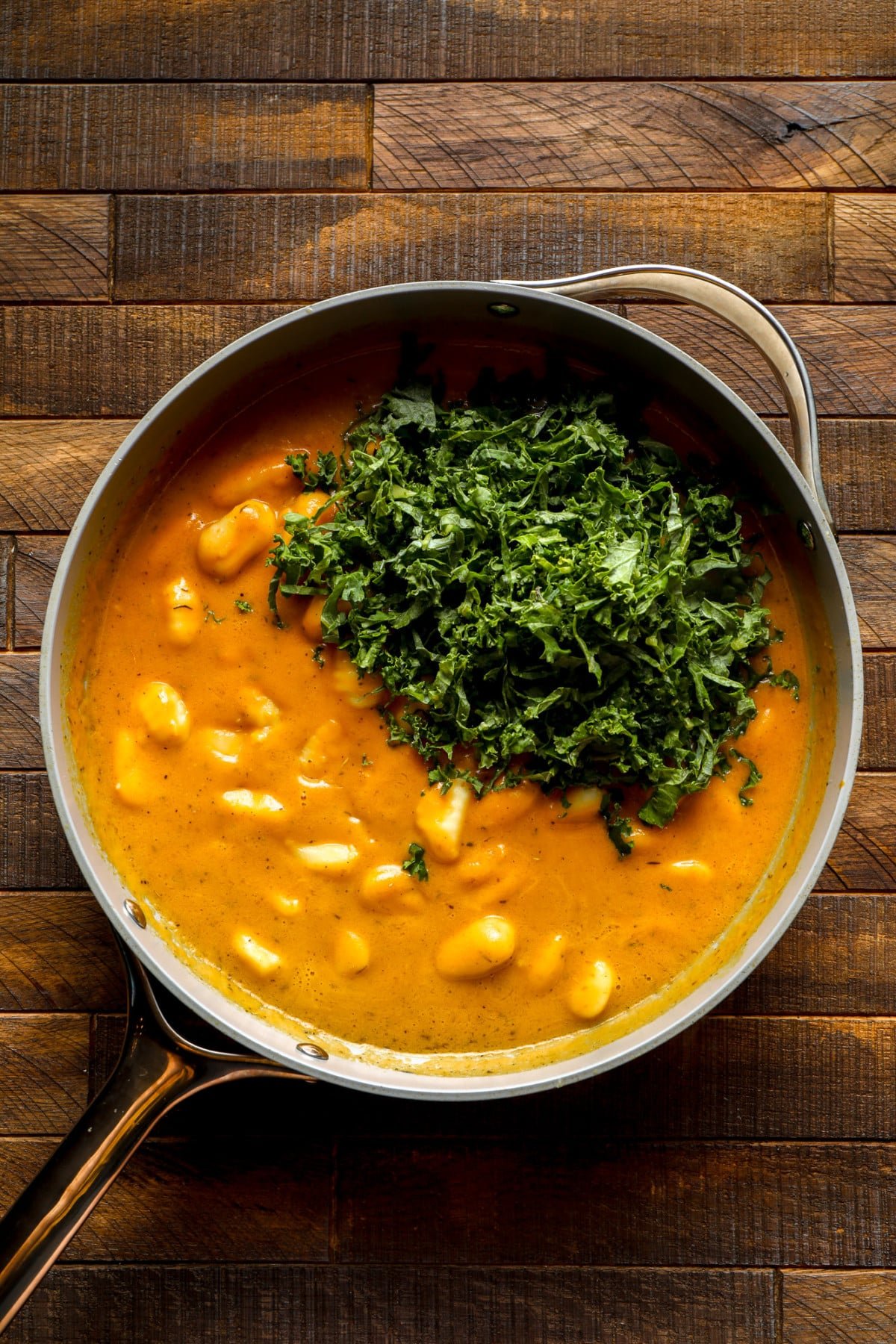 a pot of pumpkin gnocchi with chopped kale on top.