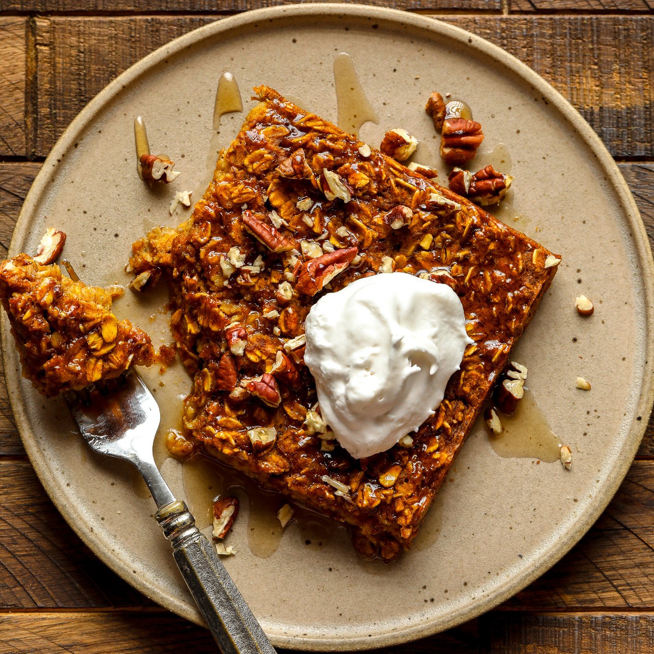 a slice of pumpkin baked oatmeal on a brown plate with a dollop of vegan whipped cream on top.