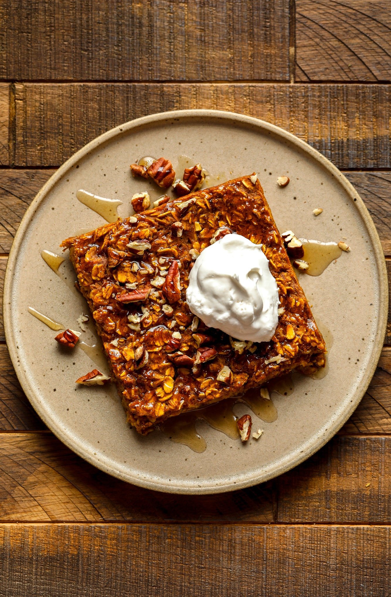 a slice of pumpkin baked oatmeal on a brown plate with a dollop of vegan whipped cream on top.