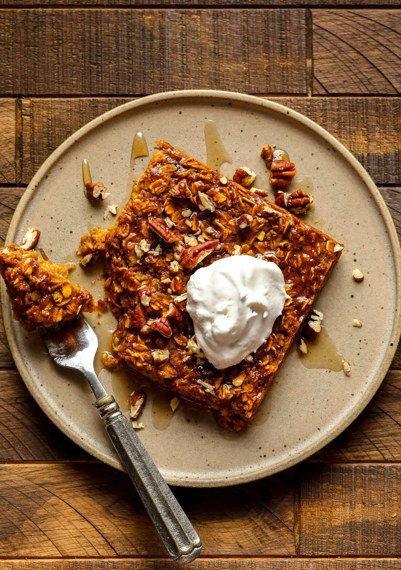 a slice of pumpkin baked oatmeal on a brown plate with a dollop of vegan whipped cream on top.