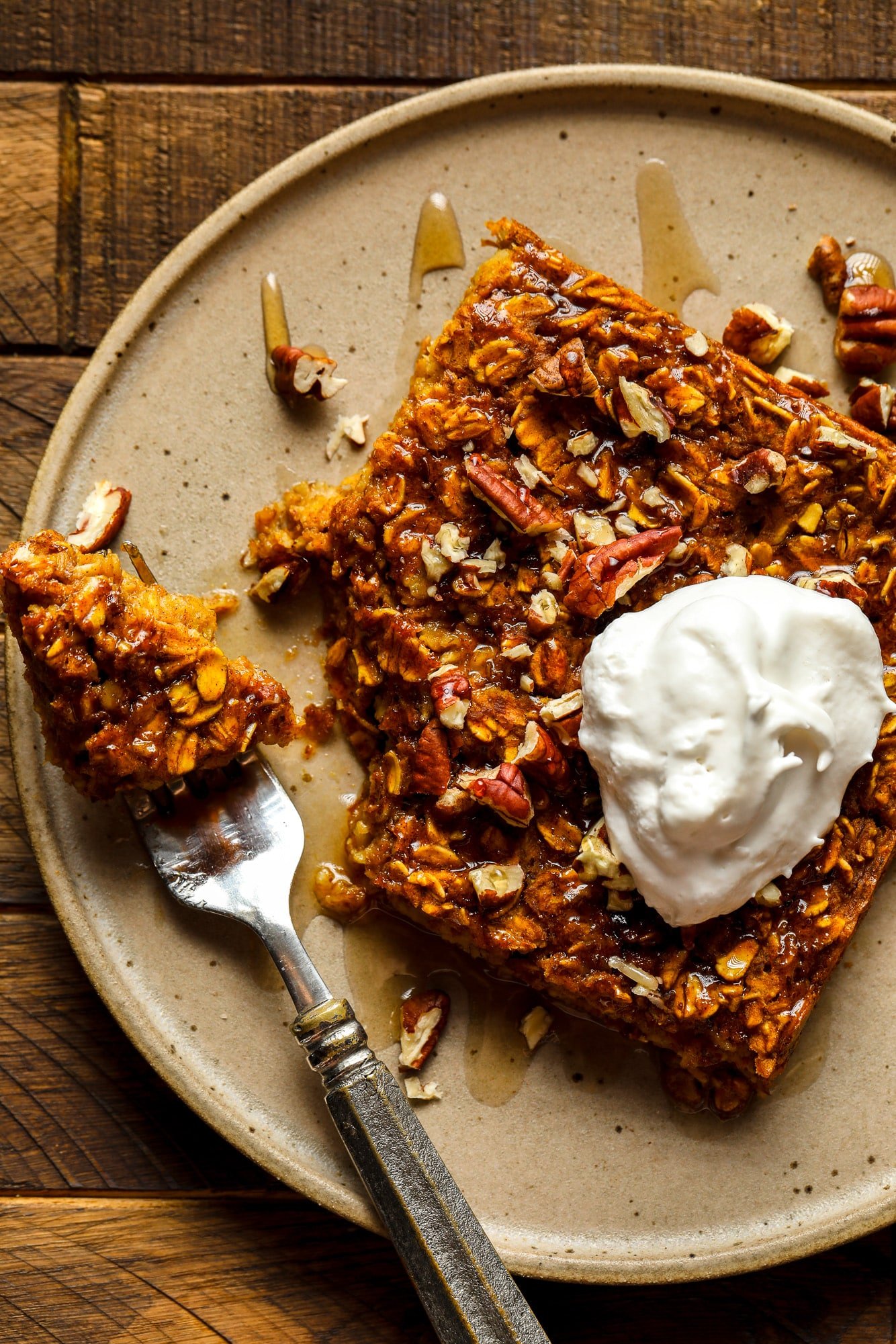 close up on a slice of pumpkin baked oatmeal on a brown plate with a dollop of vegan whipped cream on top.