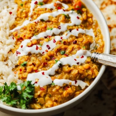 close up on red lentil dahl topped with a drizzle of coconut milk and red chili flakes in a white bowl.