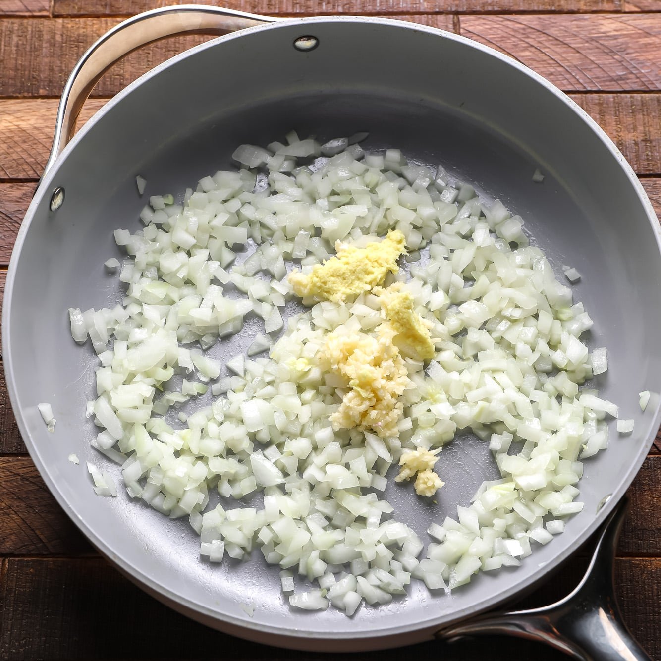 cooking chopped onions, garlic, and ginger in a large grey pan.