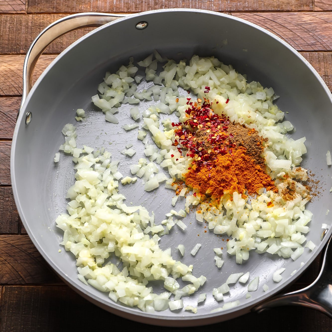 dry spices on top of cooked onions in a large grey pan.