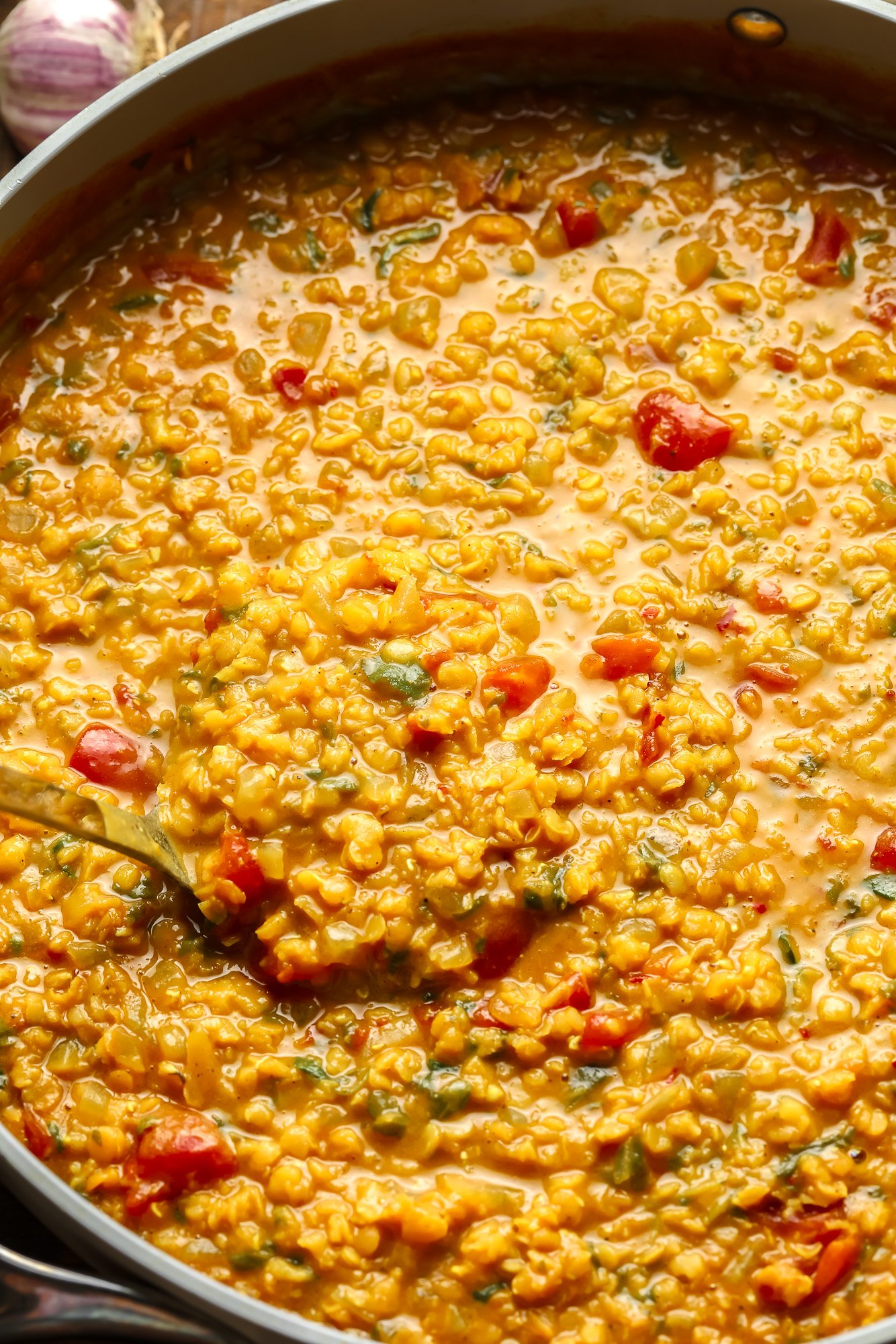 using a spoon to lift a scoop of red lentil dahl from a large pot.