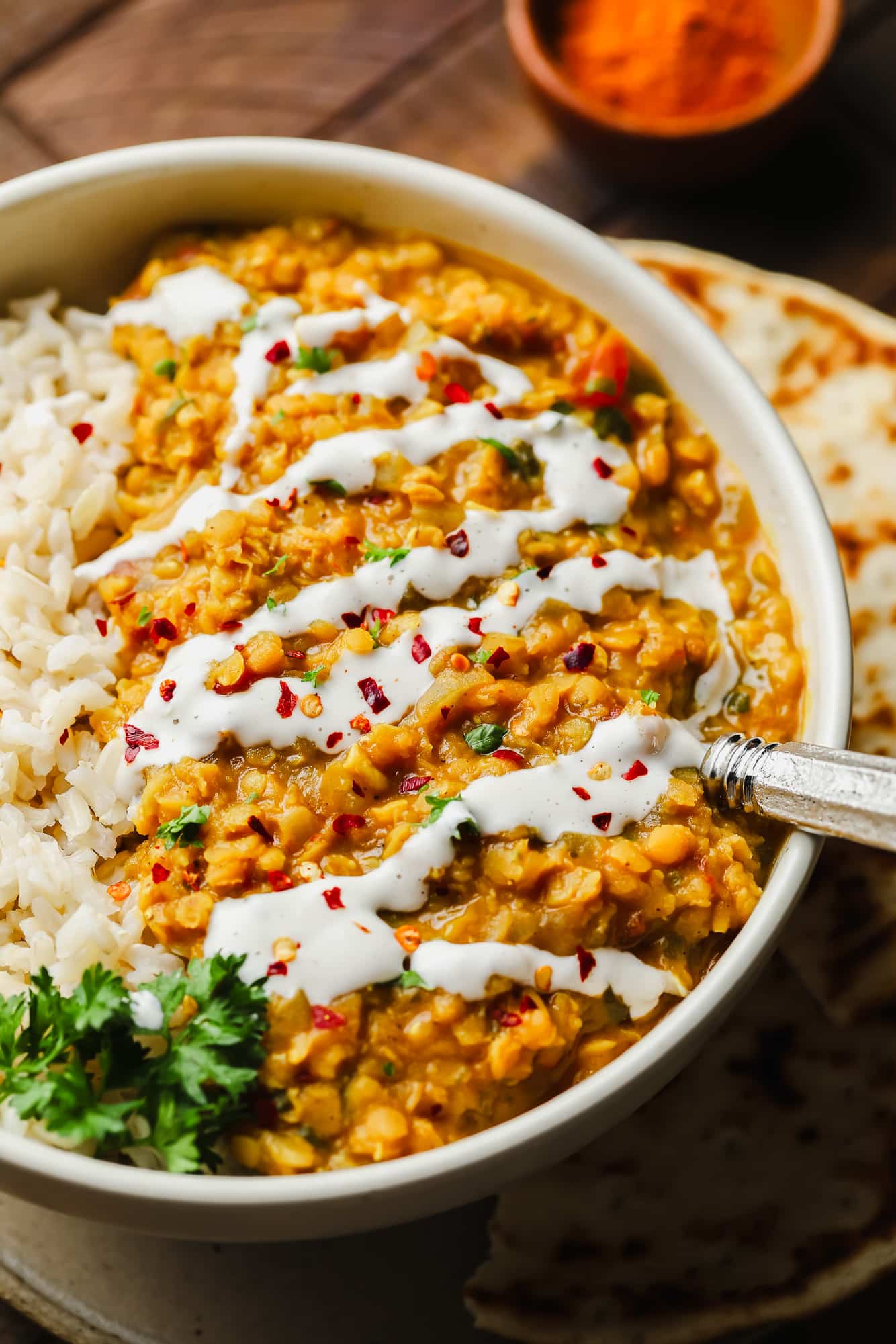 close up on red lentil dahl topped with a drizzle of coconut milk and red chili flakes in a white bowl.