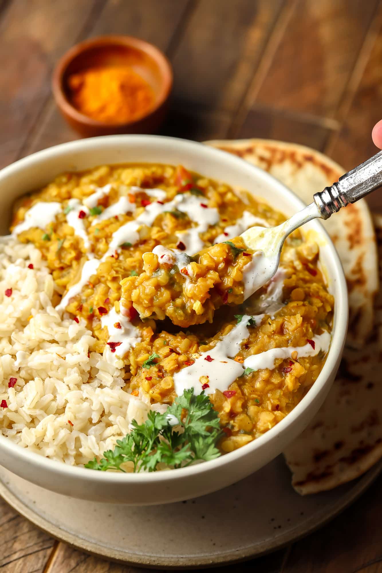 using a fork to remove a scoop of red lentil dahl from a white bowl.
