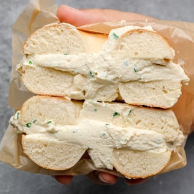 close up on a womans hand holding a vegan cream cheese bagel cut in half.