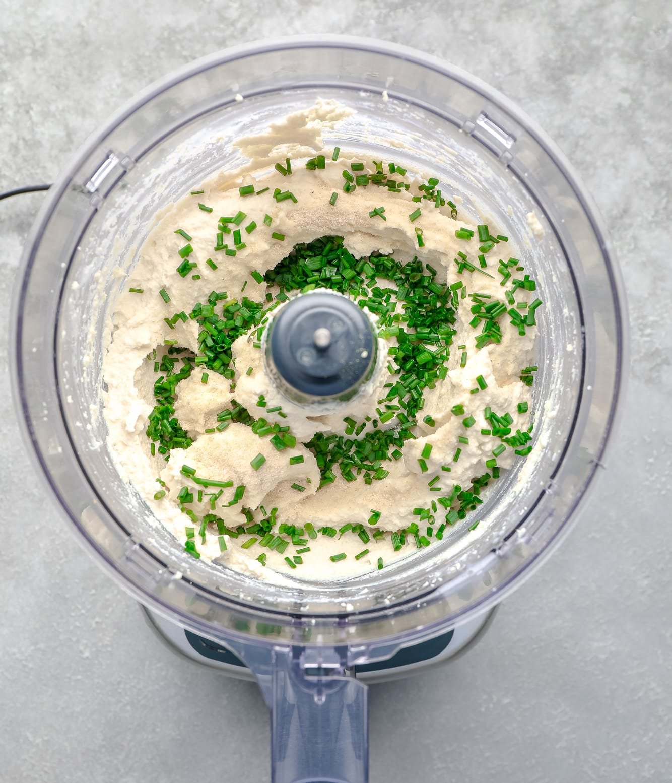 chopped chives on top of tofu cream cheese in a food processor.