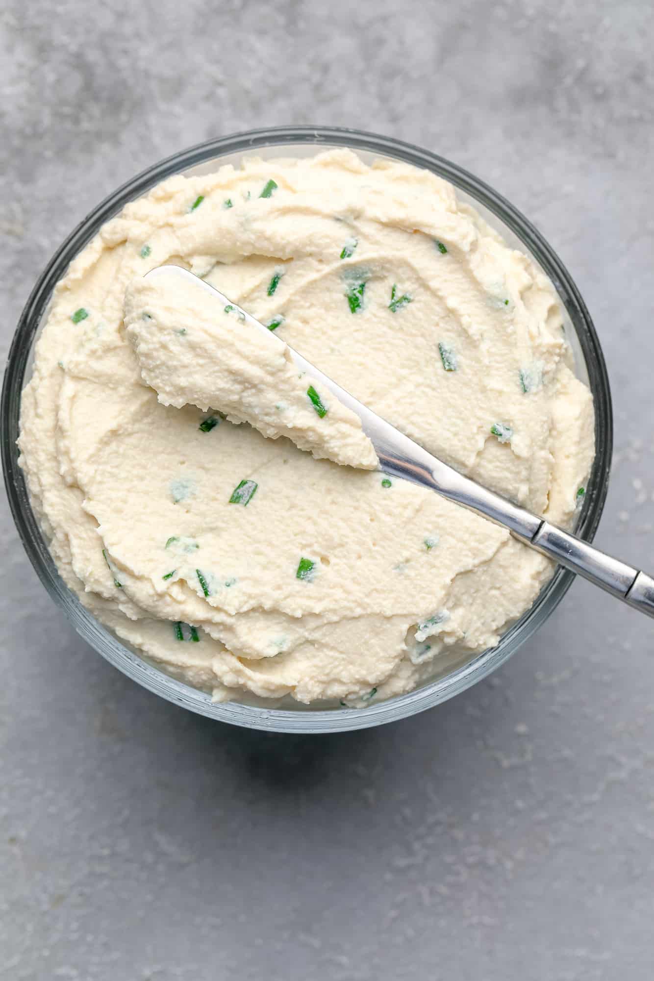tofu cream cheese in a glass container with a knife resting on top.