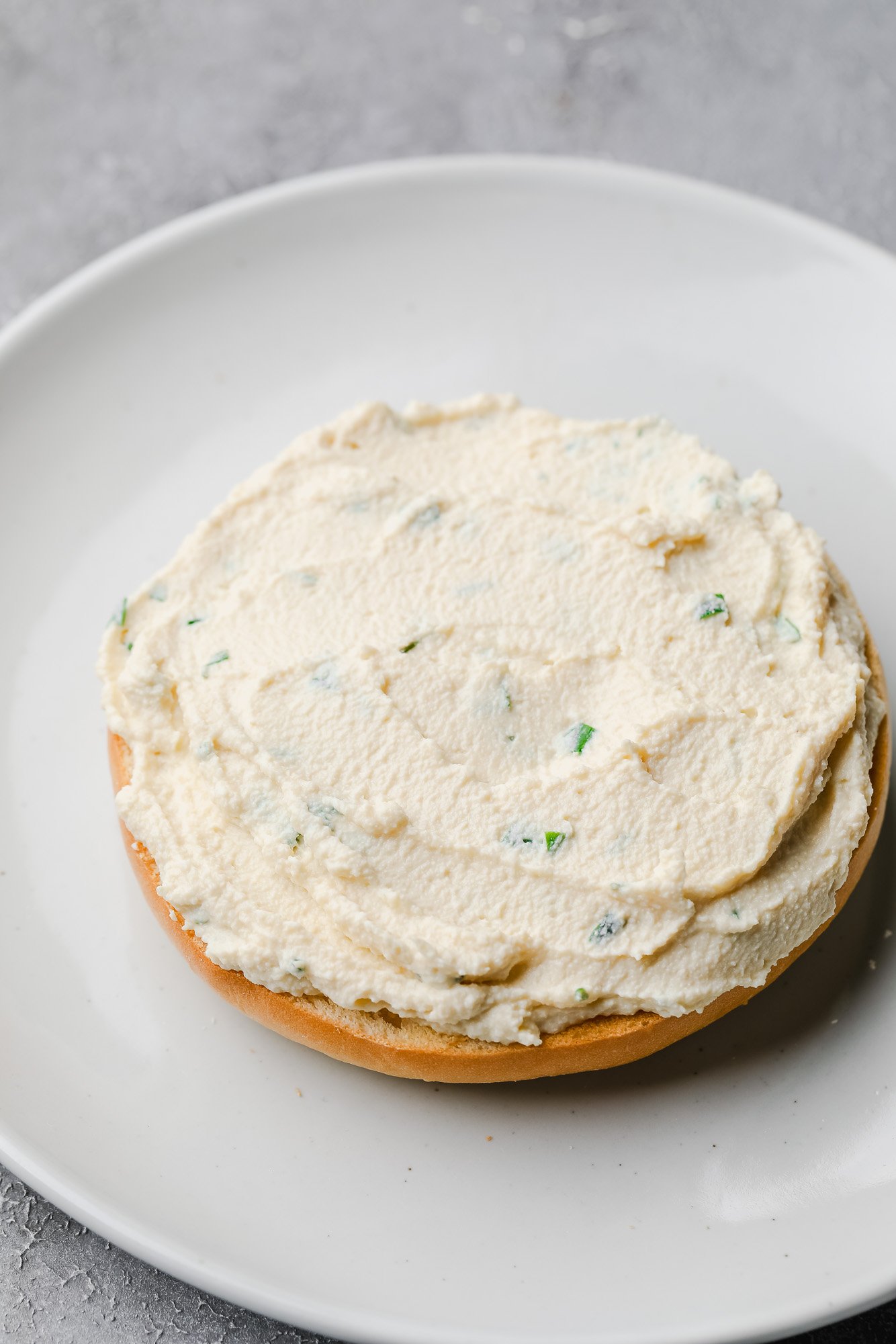 a bagel on a white plate topped with a generous amount of tofu cream cheese.