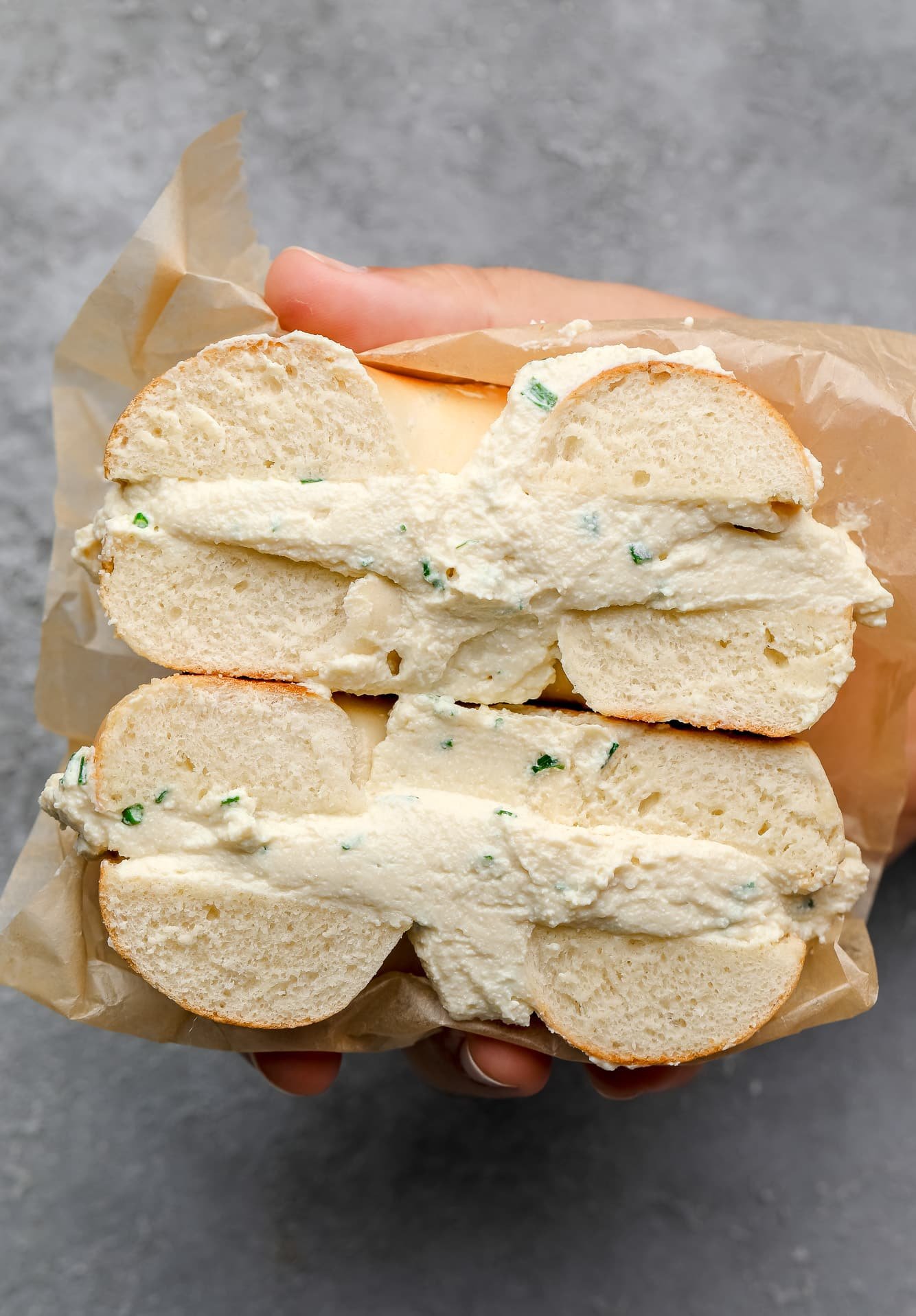 womans hand holding a vegan cream cheese bagel cut in half.
